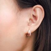 Fine jewellery, silver jewellery plated with rose gold, hypoallergenic, tarnish-free, close-up front view of a Pair of rose gold crystal earrings, Close-up front view of an ear wearing a rose gold crystal hoop earring with a blurred background